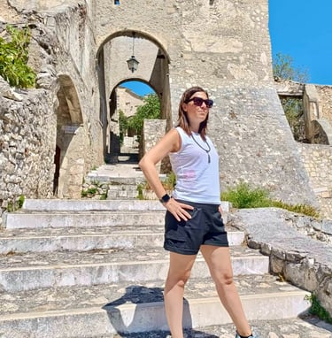 A woman in sunglasses standing on stone steps in an old Italian village with ancient arches.