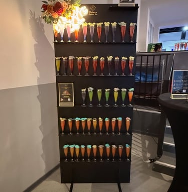 A tiered cocktail display wall at a bar featuring rows of colorful welcome drinks for a party or event.