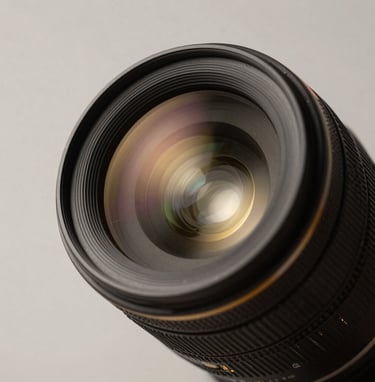 A close-up shot of a high-end professional camera lens reflecting a soft off-white studio light in a Turkish / Istanbul photography studio. Minimalist composition with deep charcoal black and metallic warm gold highlights.