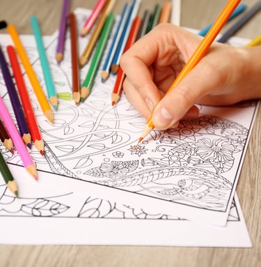 Hand using a colored pencil to fill in a detailed floral adult coloring book page.