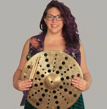 Rachel holding a cymbal with holes through out it, smiling 