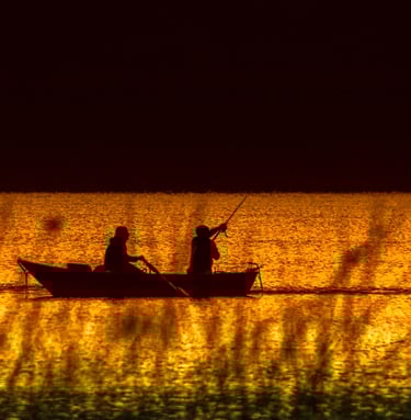 two people fishing in a lake at sunset