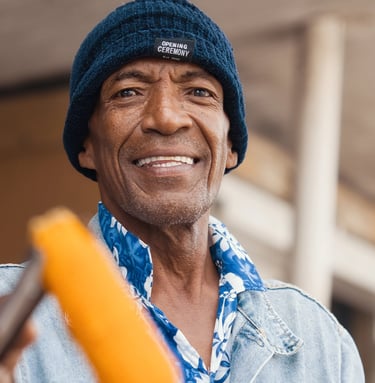 Man in a beanie hat smiling while holding roasted corn in Rodrigues.