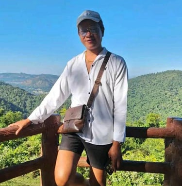 Man standing by a wooden railing overlooking green hills and blue sky in Pattaya, Thailand.