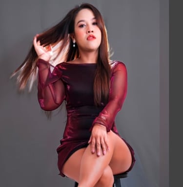 A lady sitting on a stool cross legged wearing a short long sleeve burgundy dress