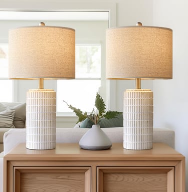A pair of modern white textured ceramic table lamps with linen shades on a wooden sideboard.
