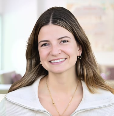 Professional headshot of a smiling woman with brown hair wearing a white sweater and gold jewelry.