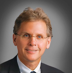 Professional headshot of a smiling male executive wearing glasses and a business suit.
