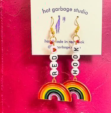 Gold huggie-hoop dangle earrings with beads that spell “red hook” and rainbow charms