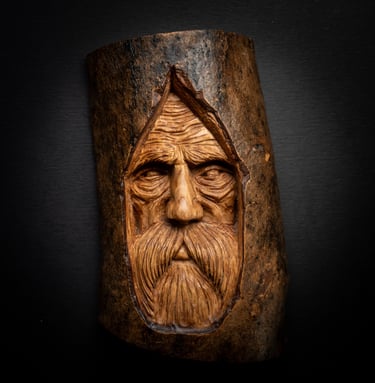 Hand-carved wood spirit face with a long beard sculpted into a natural tree log.