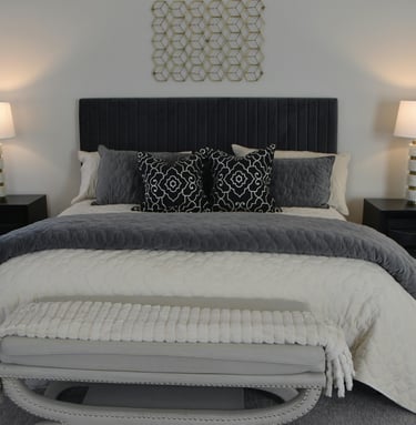 Layered bed with dark upholstered headboard, charcoal and cream bedding, patterned throw pillows, an