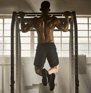 A muscular man performing wide-grip pull-ups on a power rack in a home gym for back strength training.