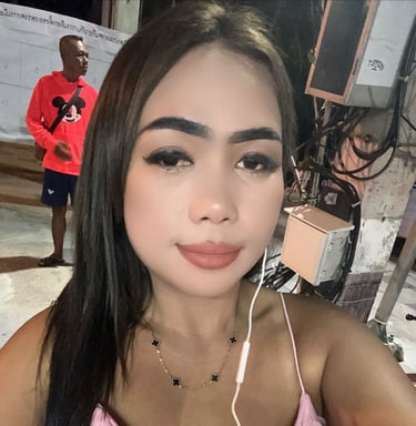 Lady wearing a pink top with headphones in left ear and a man standing in the background