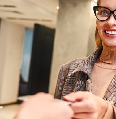 a woman in glasses and a suit jacket is smiling and holding a phone