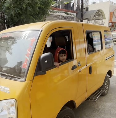 A young child in a red hoodie looking out of a yellow Mahindra Maxximo mini van on a city street.