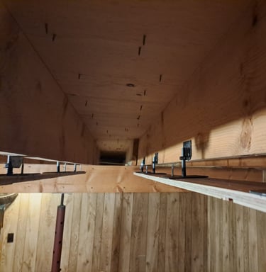 Adjustable metal brackets installed between wood joists for precision ceiling levelling in basement renovation