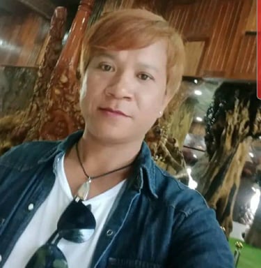 Man smiling indoors in Pattaya, Thailand, wearing a denim shirt and sunglasses on a white T-shirt.