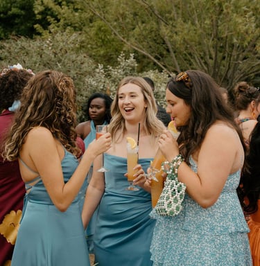 Bridesmaids in blue dresses enjoy cocktails during an outdoor wedding garden party.