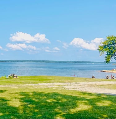 a park bench with benches and people sitting on the grass by the lake