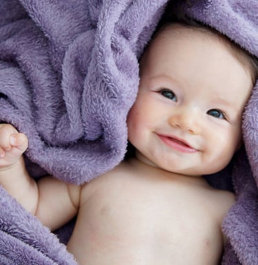 portrait de nouveau né, le bébé est souriant et enveloppé dans un tissu violet