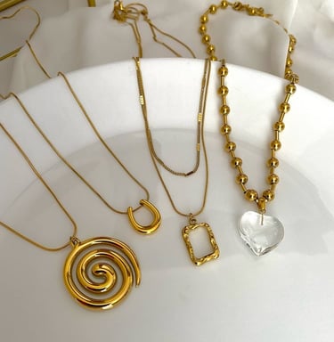 Colección de collares de oro con diseños de espiral, herradura y corazón de cristal en placa blanca