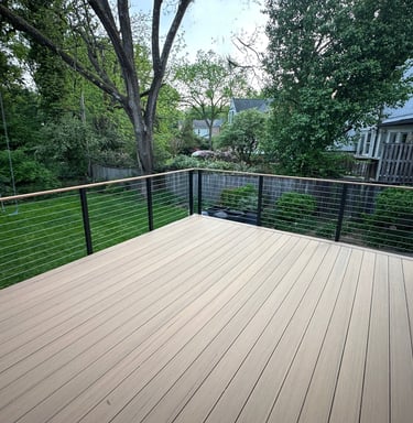 Modern composite deck with horizontal cable railing overlooking a lush green backyard and garden.