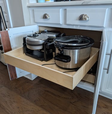 Kitchen cabinet pull-out drawer holding a crock pot and waffle maker. Easy access on display.