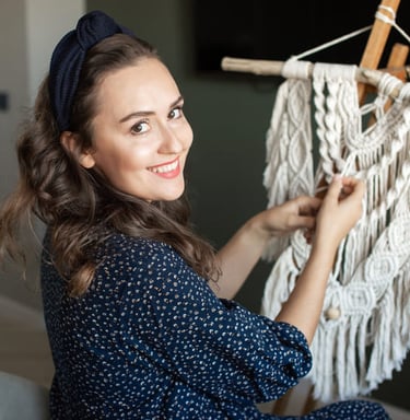 mujer sonriendo a la camara, y trabajando en un proyecto de macrame