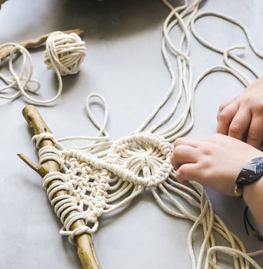 proyecto pequeño de macrame en blanco sobre un tronco de madera
