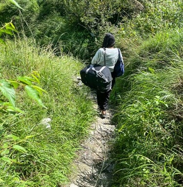 Pooja with large bag going down steep path.
