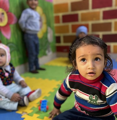 Toddlers playing in a colorful daycare center with foam mats and painted wall murals.