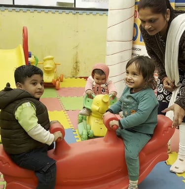 Young children playing on colorful indoor playground equipment with a teacher supervising at a daycare center.