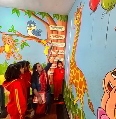 A preschool teacher pointing to a colorful giraffe height chart and days of the week mural in a classroom.