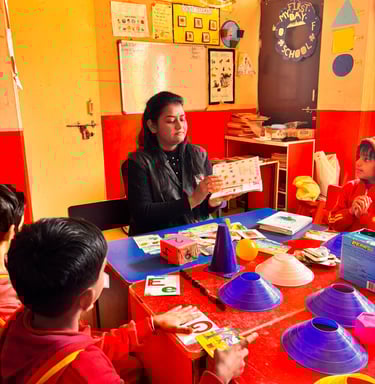 A primary school teacher shows flashcards to young students in a colorful, decorated classroom.