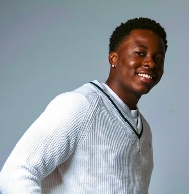 a man in a white sweater and jeans standing in front of a gray background