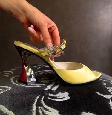 a person's hand holding a ring on Judy Mazzotti's sandal a yellow elegant shoe in silk satin 