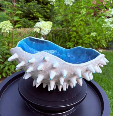 Handmade spiky ceramic bowl with white textured exterior and vibrant blue glazed interior in a garden.