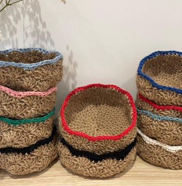Stacks of handmade small jute crochet baskets with colorful yarn rims for home storage and organization.
