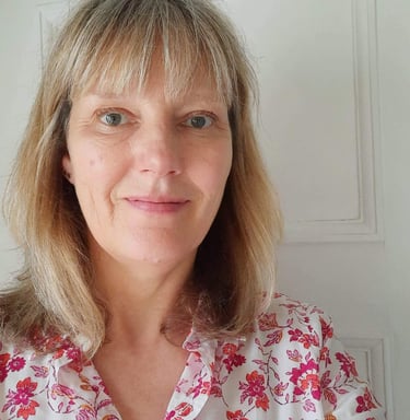 Profile of a middle aged woman with short blonde hair wearing a floral pink shirt