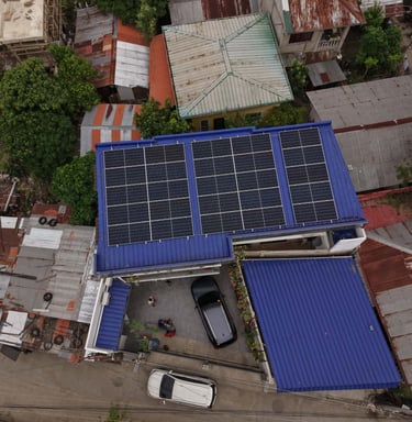 Aerial view of residential solar panels installed on a blue metal roof in an urban neighborhood.