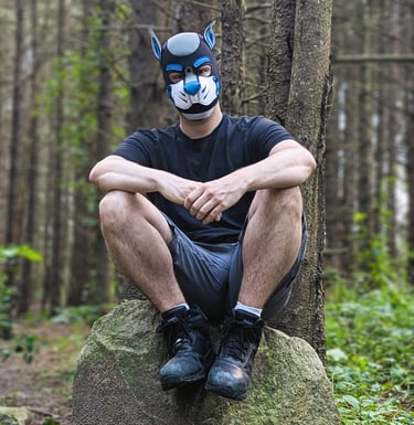 A man sitting in the woods wearing a pup mask.