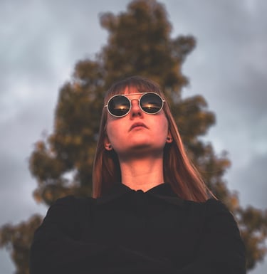 a women in a black jacket and sunglasses staring into the sunset