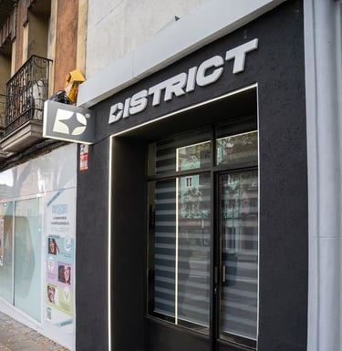 Fachada moderna y oscura de la barbería DISTRICT en Madrid, mostrando el logo y la entrada principal