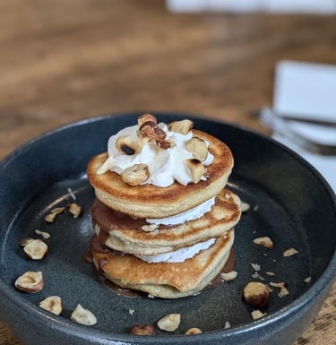 une assiette sur une table en bois avec une tour de pancakes et chantilly