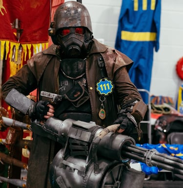 A man in a Fallout game costume stands with a large prop weapon and mask