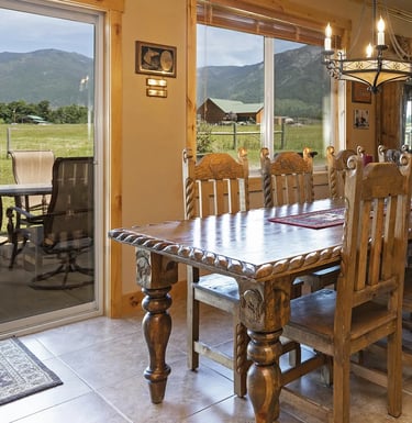Dining room table on stone tile floors. Wood trim on walls. Mission mountains out the window.