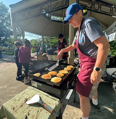 Kids in the background of a person flipping pancakes on a griddle in a park