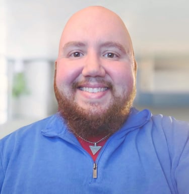 Smiling bald man with a red beard wearing a blue quarter-zip pullover and a silver necklace.