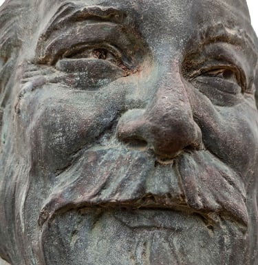 Bronze relief bust of a bearded man mounted on a natural stone rock in an outdoor park setting.
