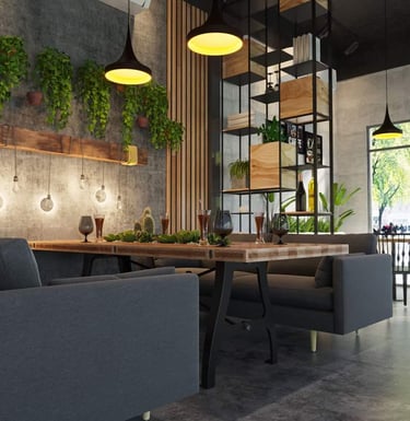 Modern cafe interior with industrial decor, hanging plants, wooden tables, and grey sofa seating.
